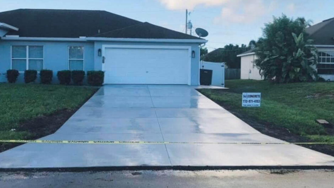 A freshly poured concrete driveway leads to a light blue house with a white garage door.