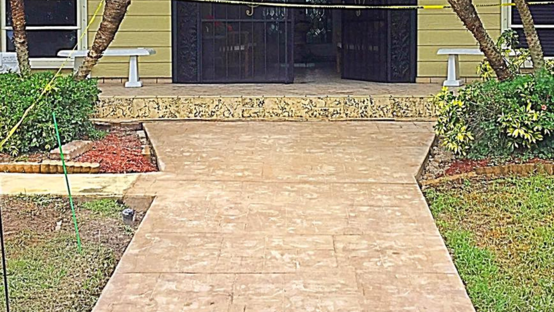 Concrete walkway leading to a building's open doorway. Landscaping on either side.