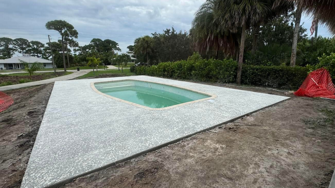 Small rectangular pool surrounded by white pebble stone, set in a yard with greenery.
