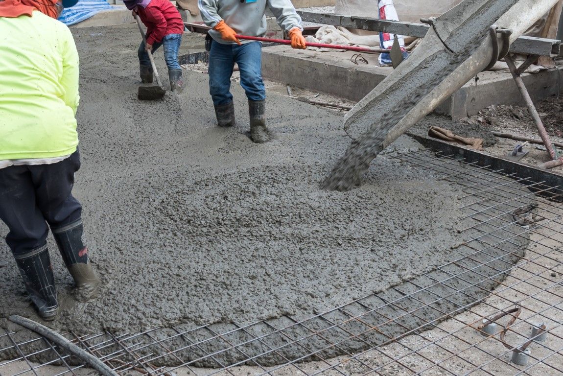 Workers pouring concrete onto rebar on a construction site.