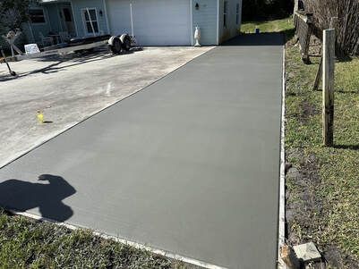 Freshly poured concrete driveway in front of a light blue house with a garage.