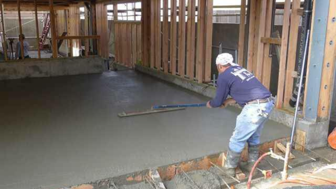 Man using a tool to level fresh concrete inside a wooden structure.