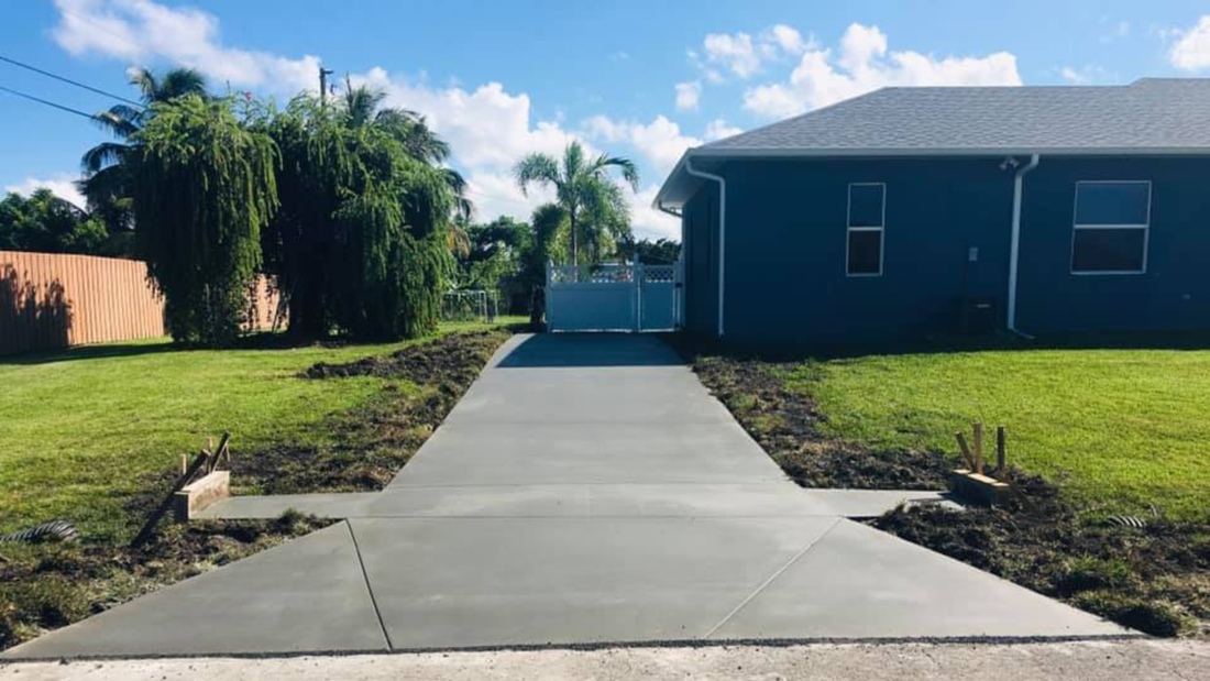 Newly poured concrete driveway leading to a blue house with green grass and trees.