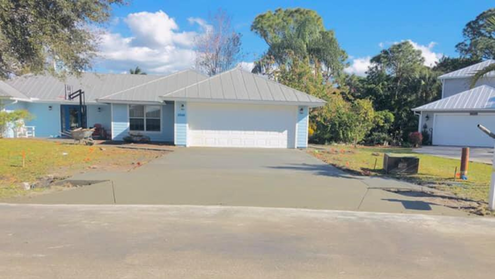 Blue house with new concrete driveway under a blue sky, two-car garage.