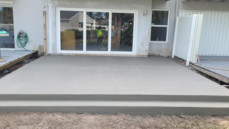 Newly poured concrete patio with steps in front of a house with sliding glass doors.