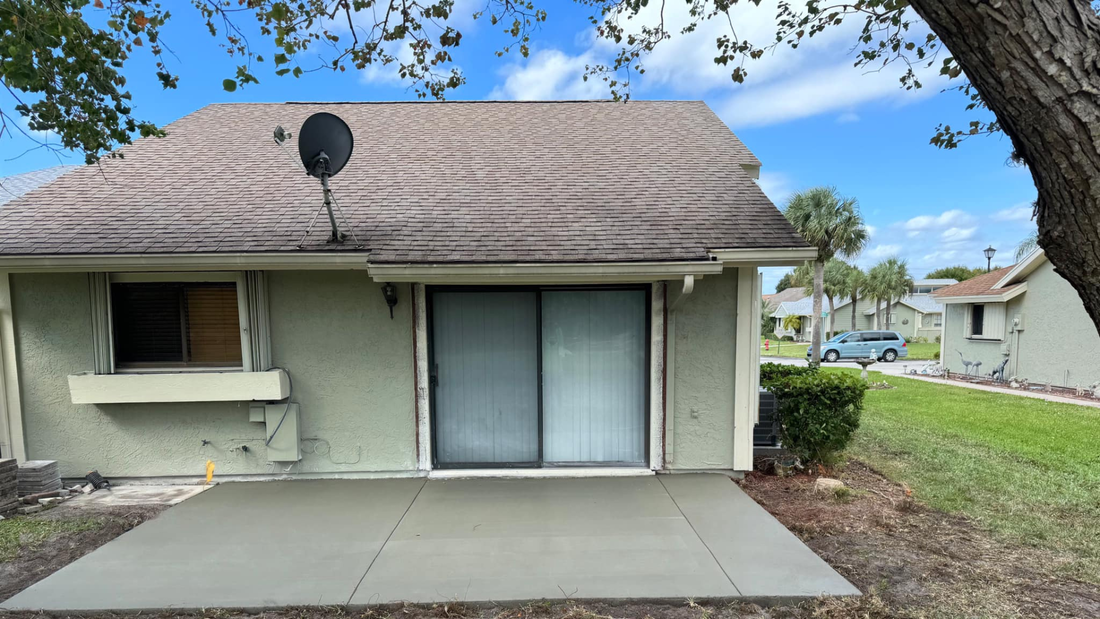 Green house with patio, sliding door, satellite dish, and overcast sky.