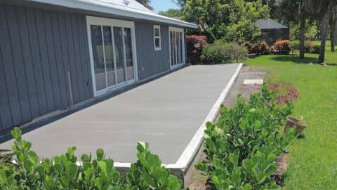 Gray deck alongside a gray house with large sliding glass doors, surrounded by green shrubs and grass.