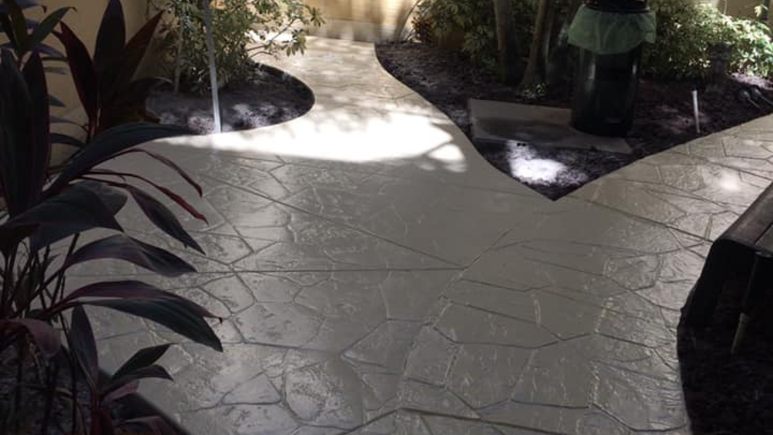 Stone pathway through a garden, shaded by plants, with sunlight illuminating the surface.