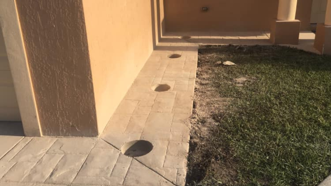 Concrete path with drainage holes next to a wall and grassy area. The path and wall are beige.