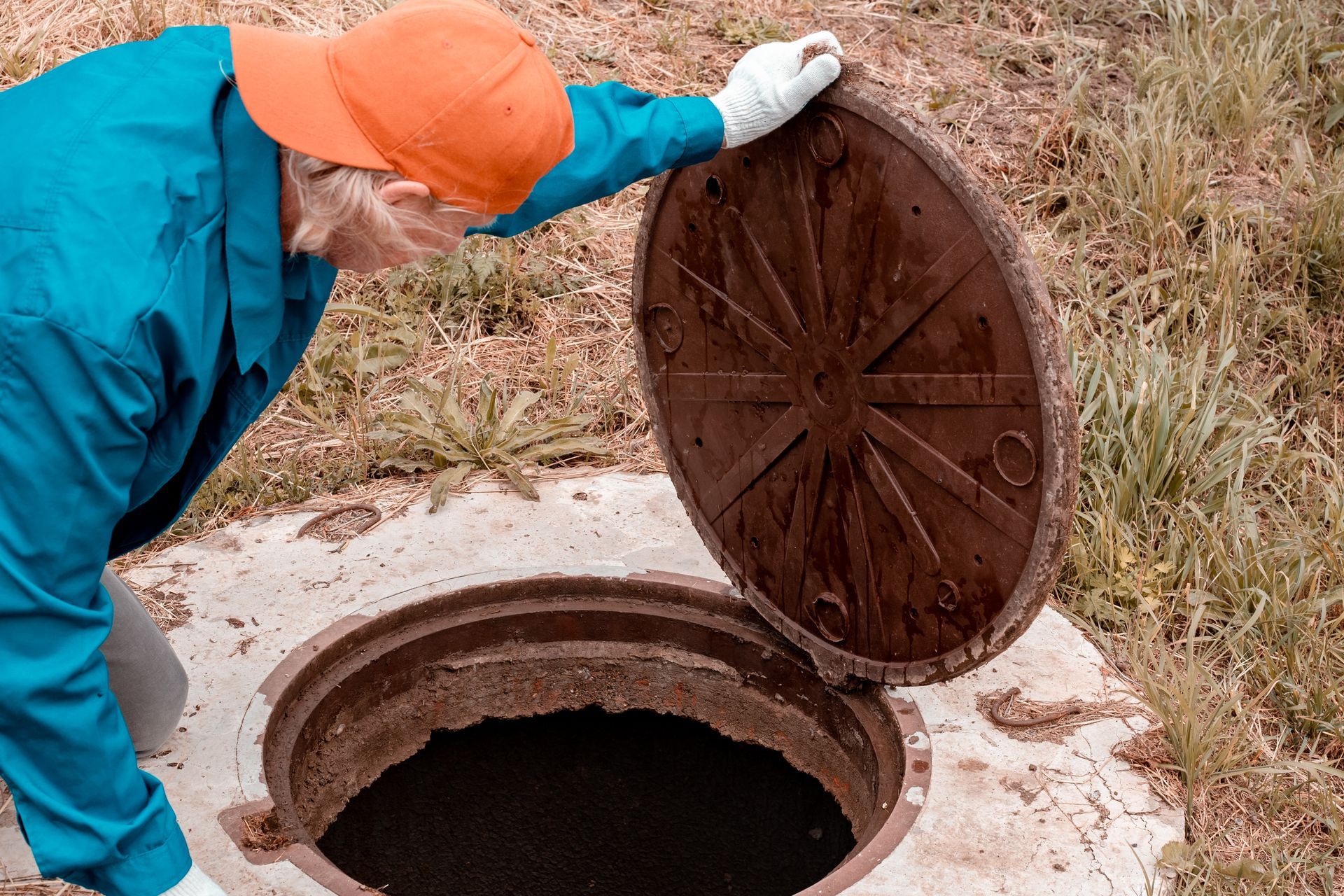 Worker lifting an open septic tank lid in a grassy outdoor area. Worker lifting an open septic tank lid in a grassy outdoor area.