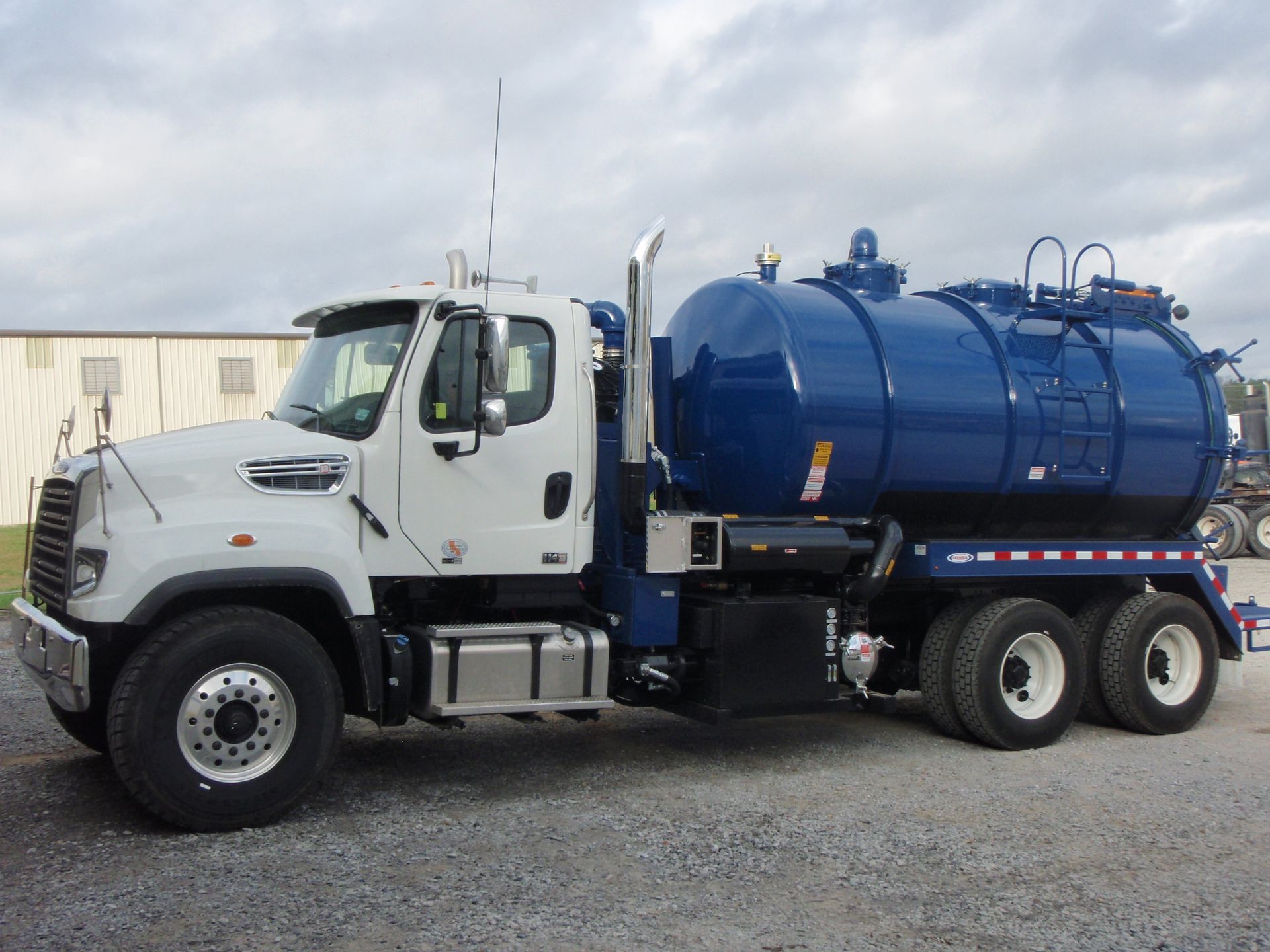 White and blue vacuum truck parked outdoors, blue tank, side view.