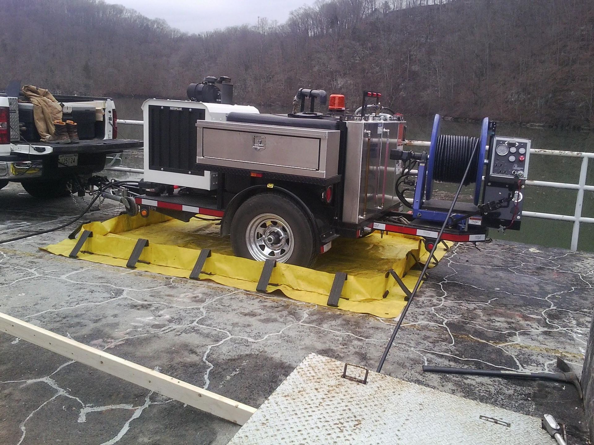 A trailer-mounted machine on a concrete structure, yellow containment berm around it, near a body of water.