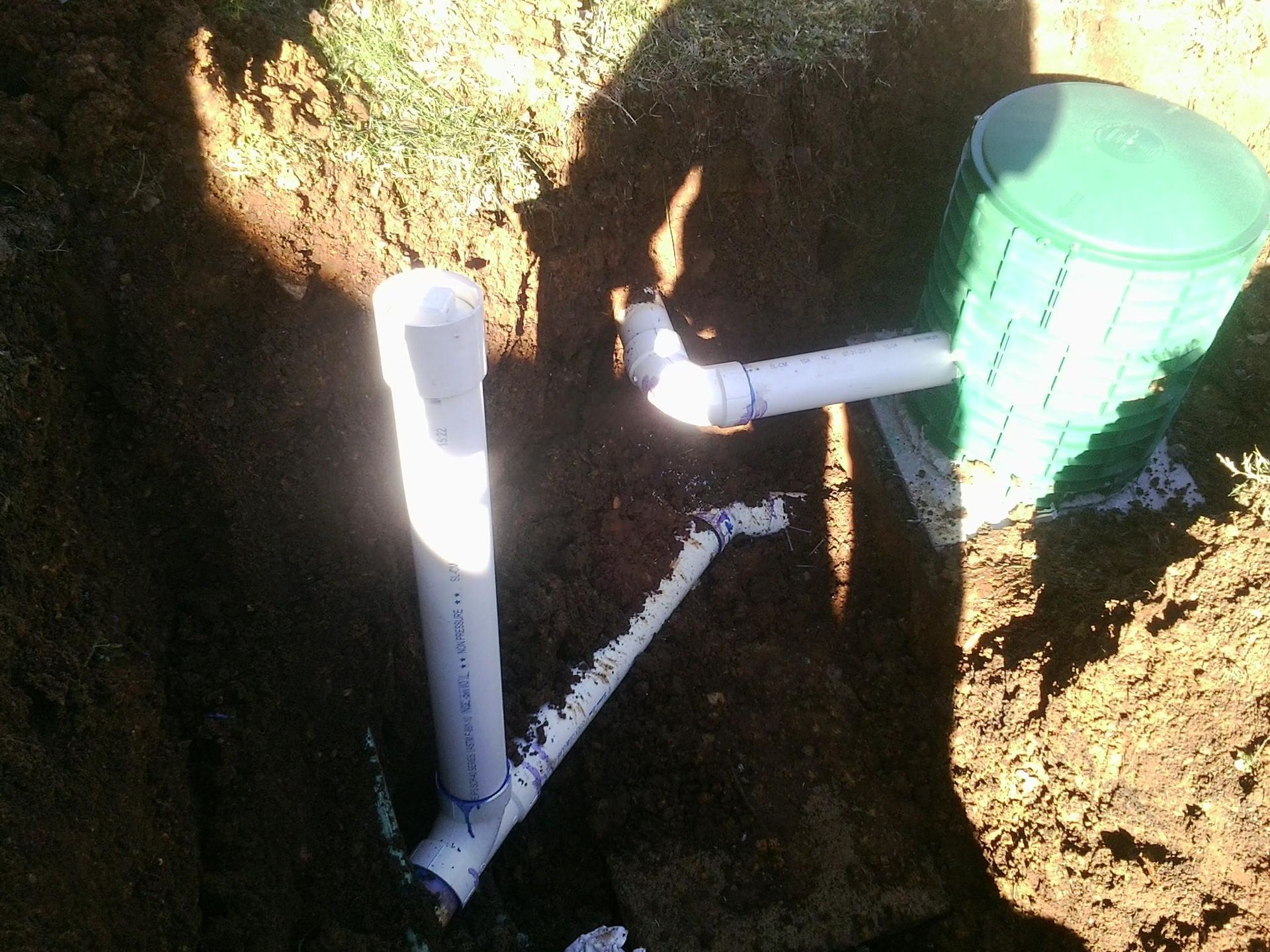 Pipes and a green container in a dirt trench, likely part of an underground plumbing or septic system installation.
