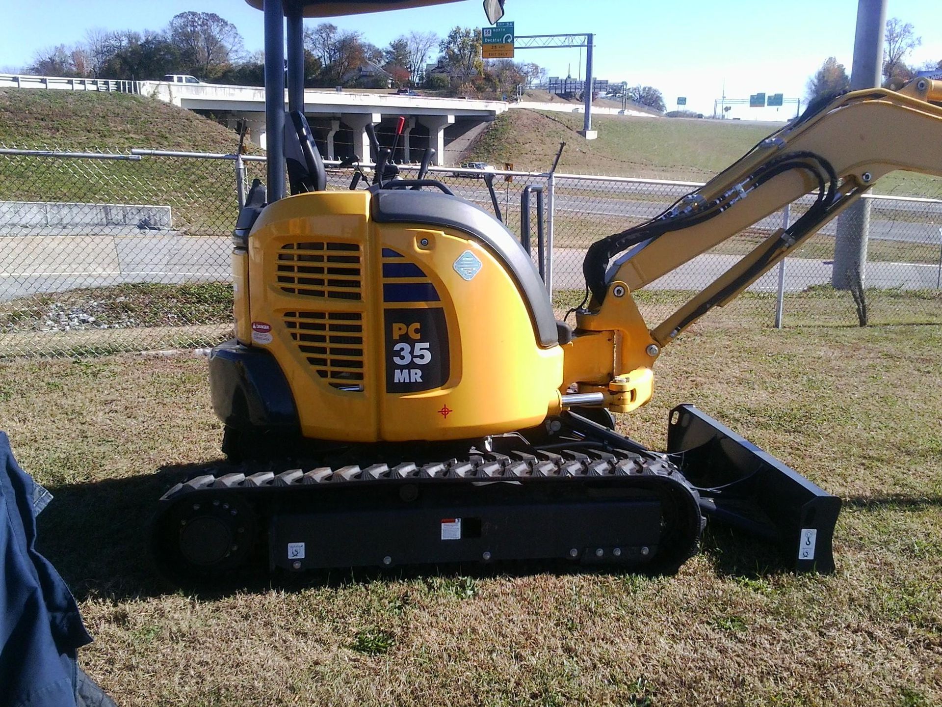 Yellow Komatsu PC35 MR excavator on grass. Highway and bridge in the background.