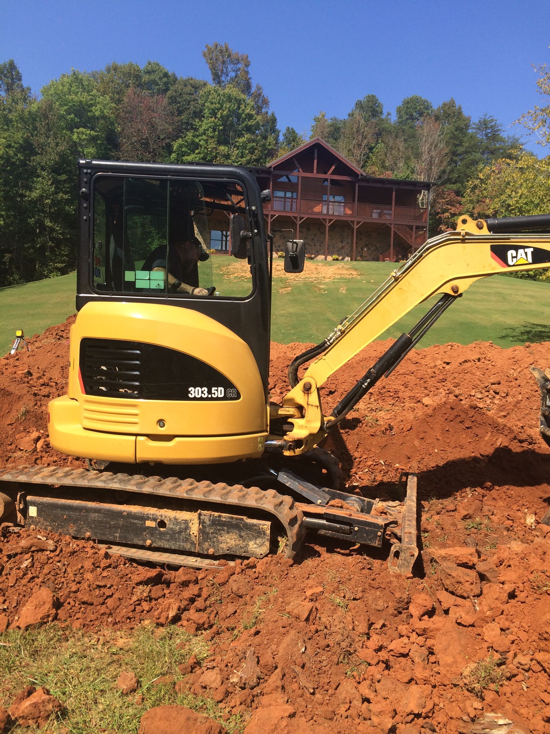 Yellow Caterpillar mini excavator on red soil in front of a house.