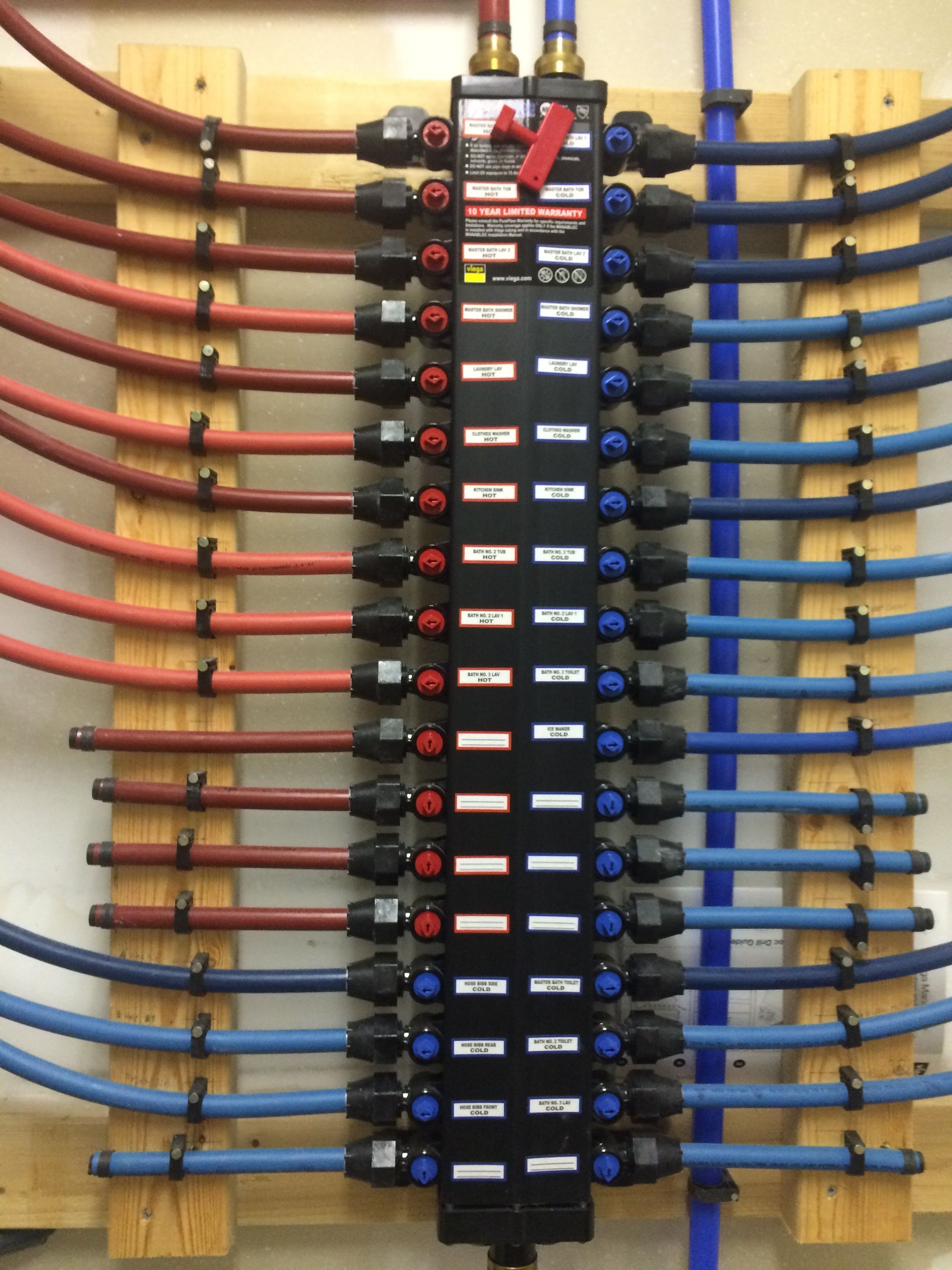 Red and blue pipes connected to a black manifold on a wooden frame for a radiant heating system.