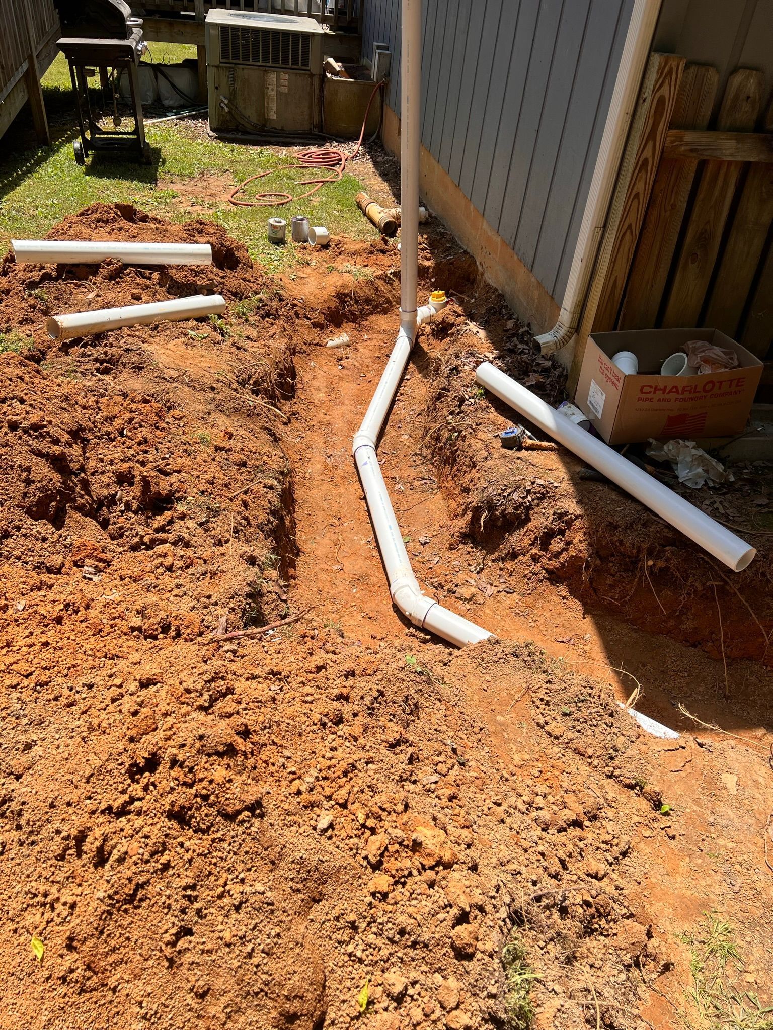 PVC pipes in a trench, next to a building. Brown dirt, daylight, outdoor setting.