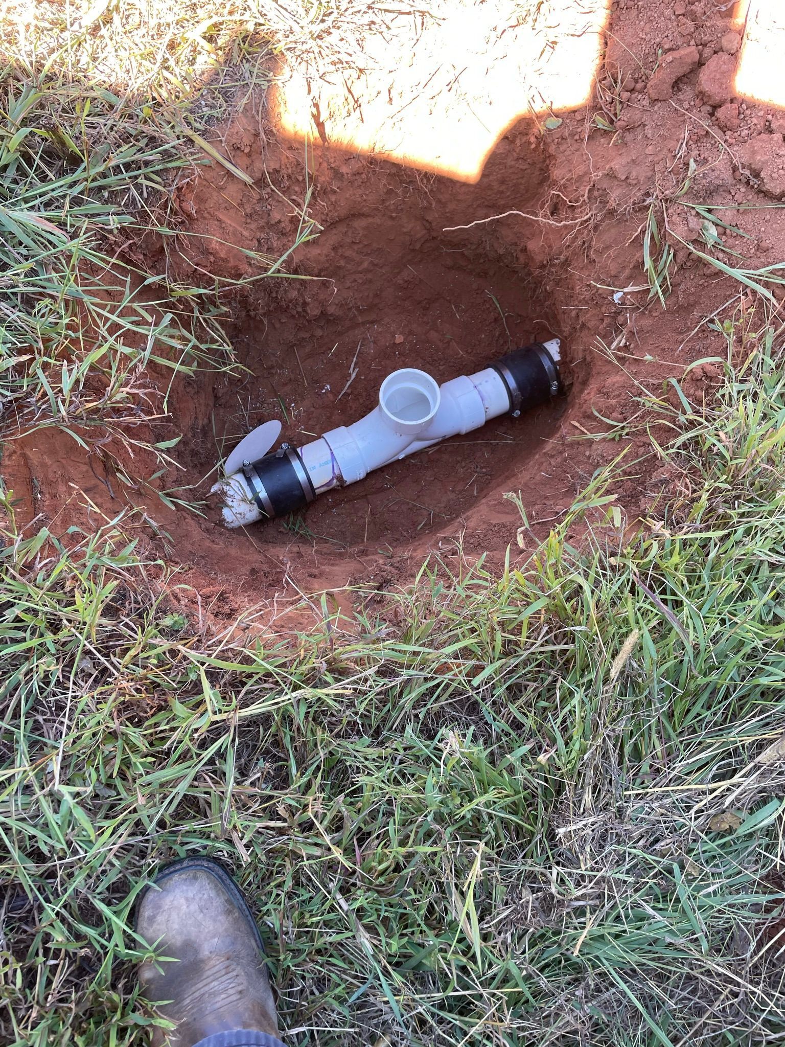 PVC pipe with a valve in a hole in the ground, surrounded by grass and dirt.