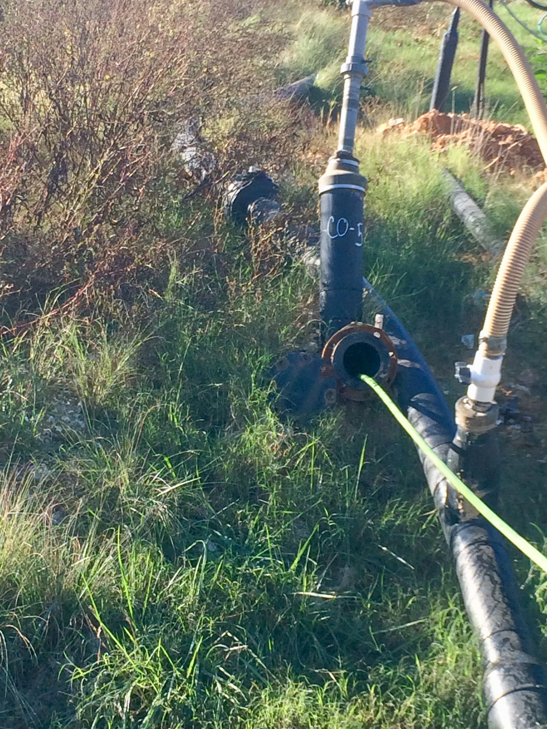 Black pipe and fittings with green cable, in grassy outdoor setting.