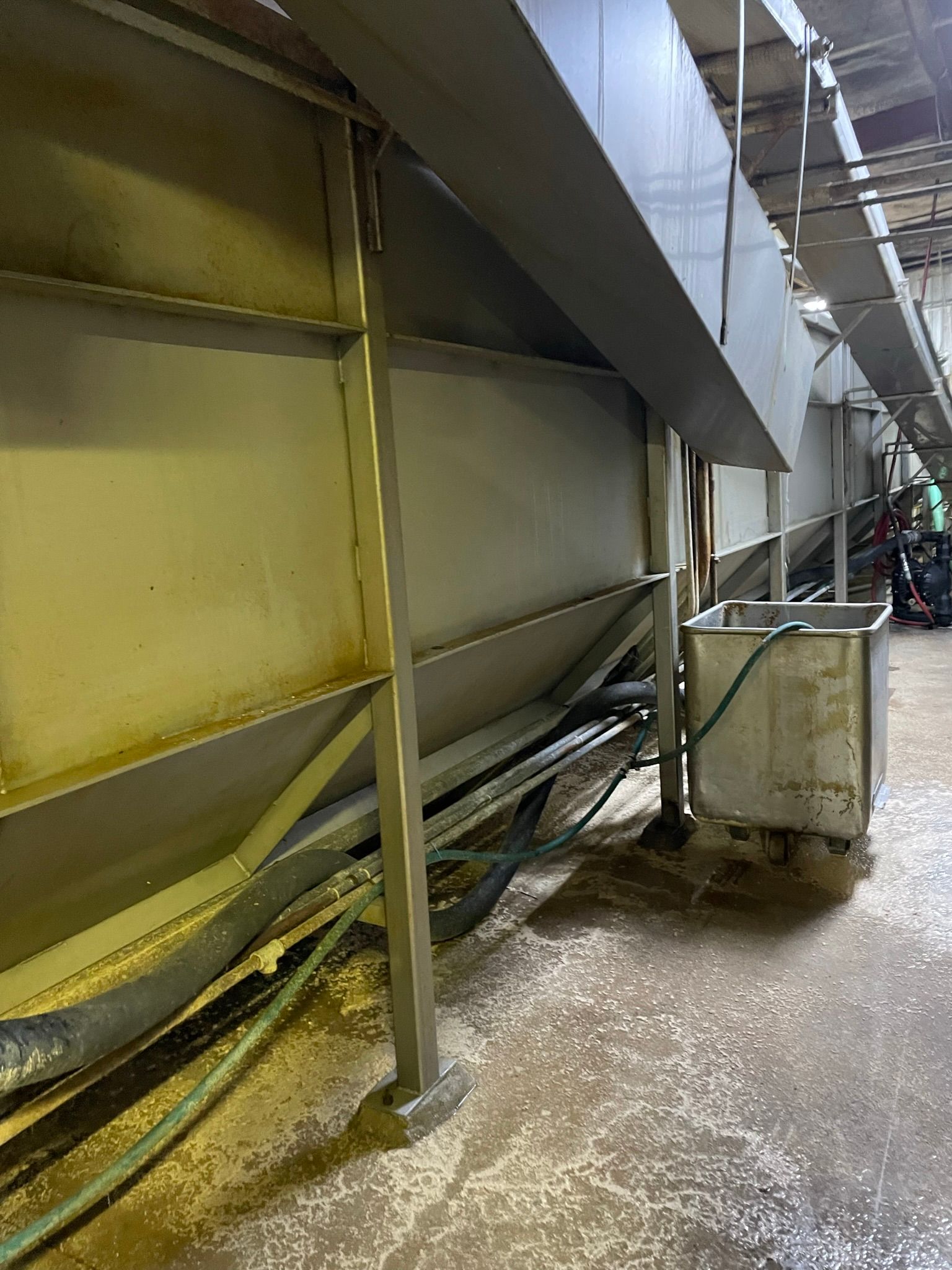Industrial area with metal machinery, pipes, and hoses near a concrete floor.