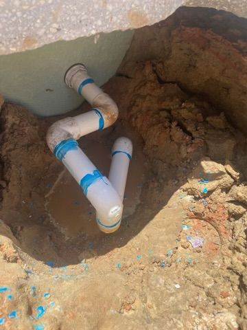 White and brown PVC pipes bent in a zig-zag shape inside a dirt trench.