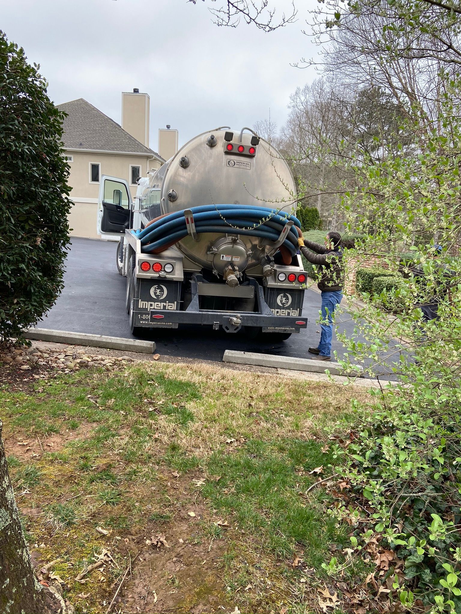 A septic tank truck parked on a driveway in front of a house; a person is working near the truck.