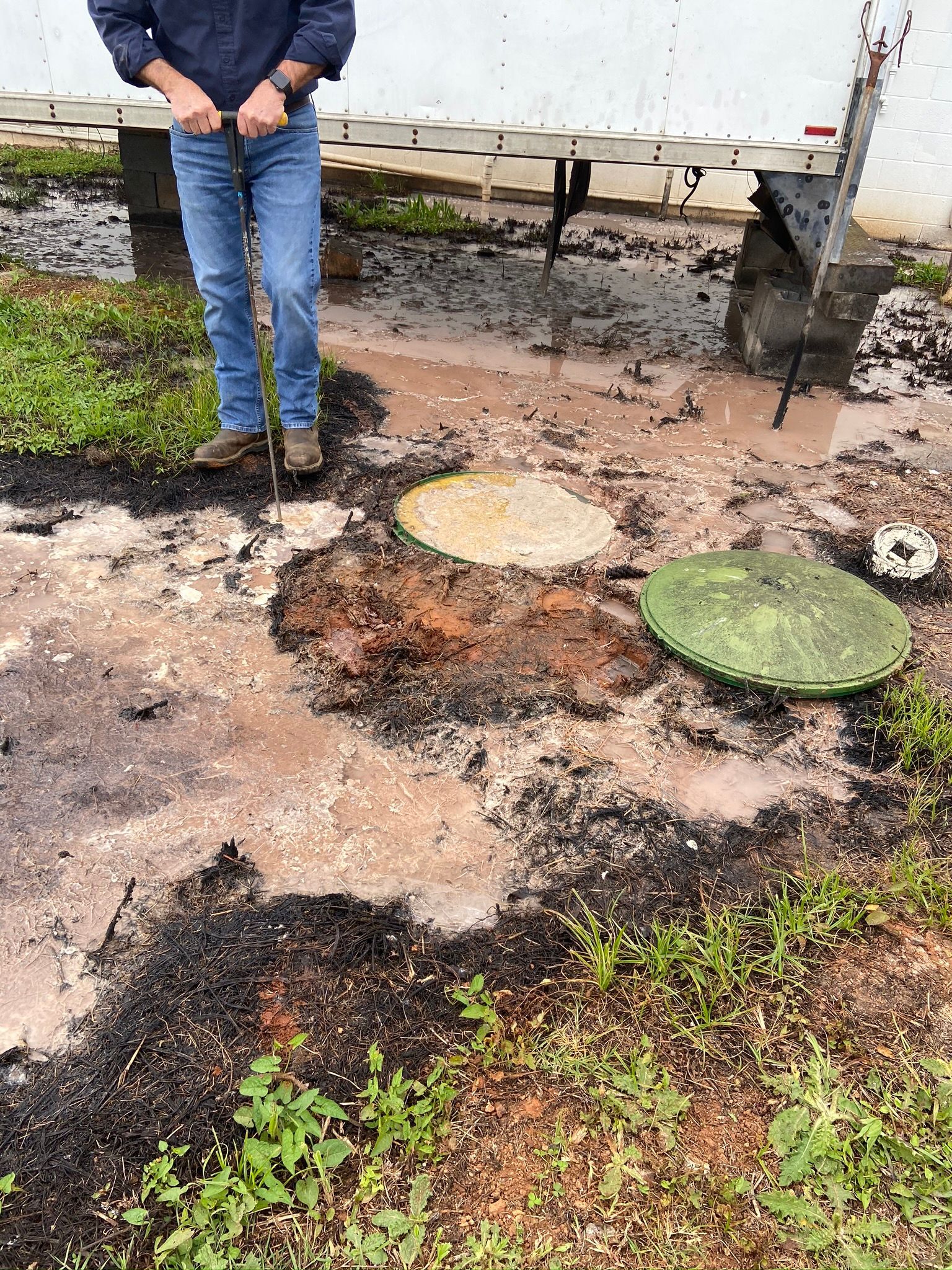 Man standing near septic tank access, surveying water and debris.