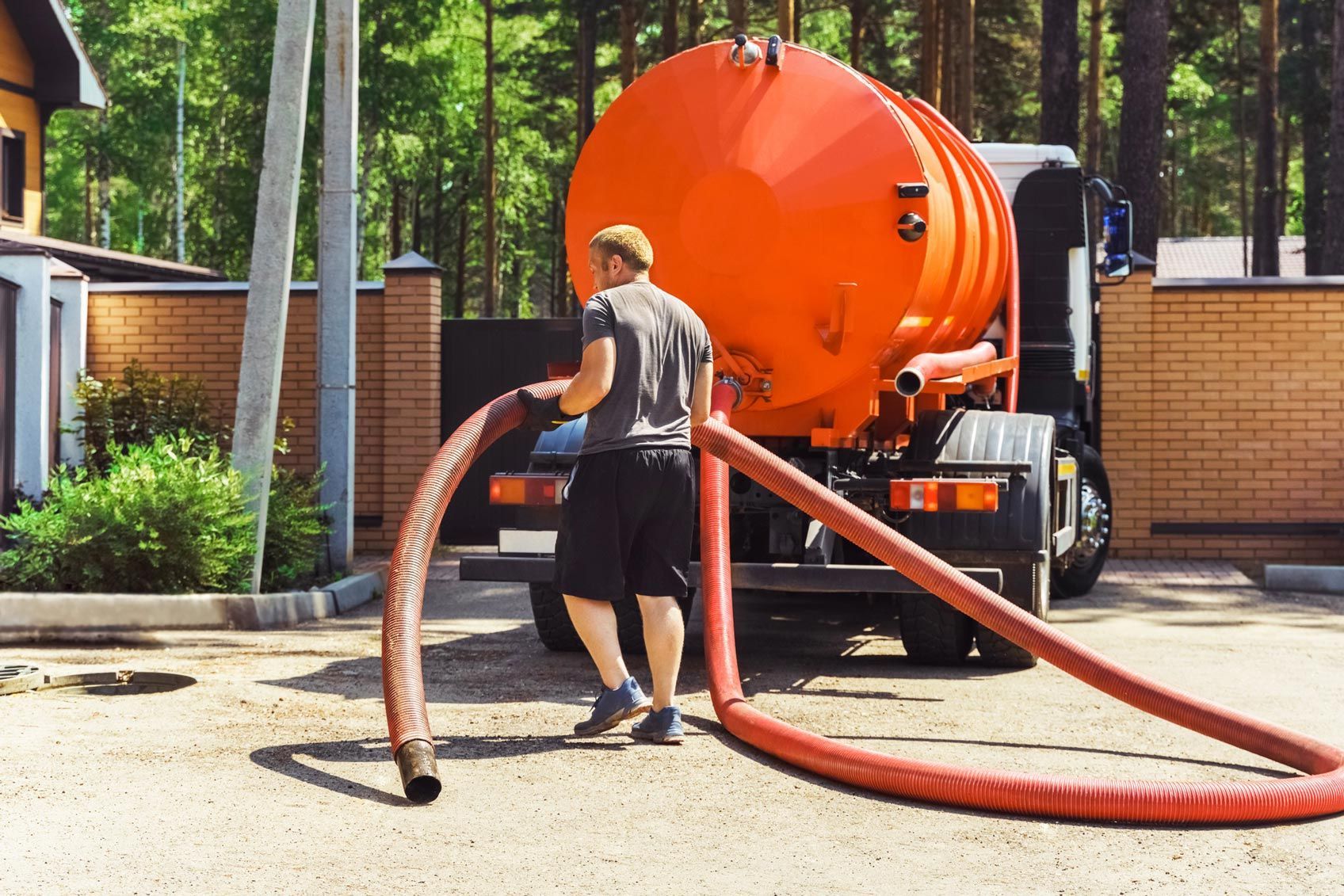Worker connects hoses to orange septic truck in residential area. Worker connects hoses to orange septic truck in residential area.