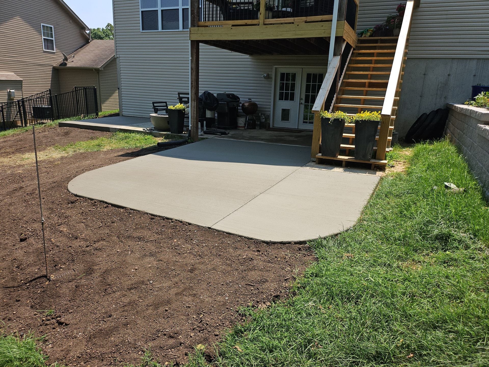 A newly poured concrete patio, with a wooden deck above, surrounded by mulch and grass.
