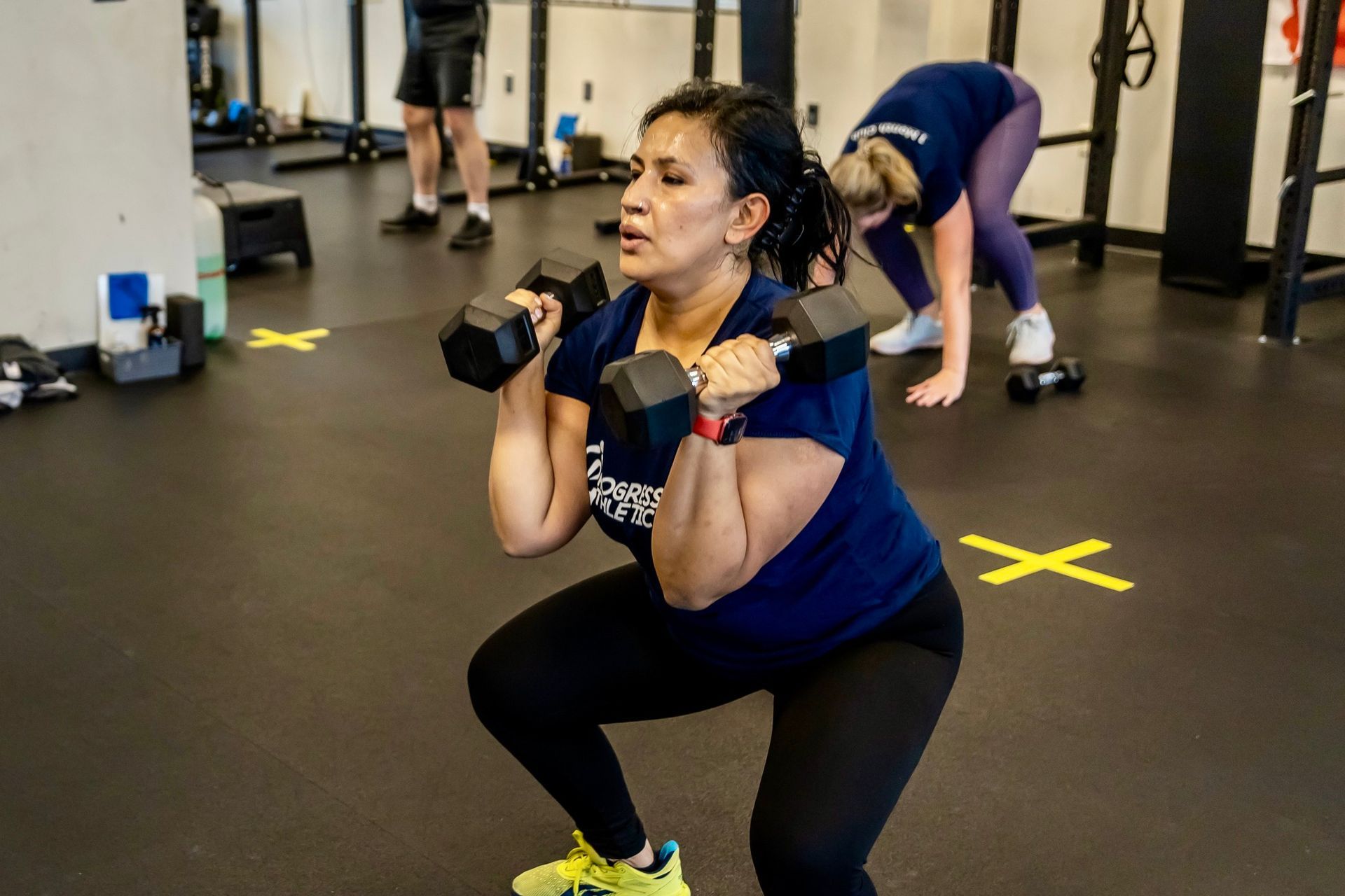 A woman is squatting with dumbbells in a gym.