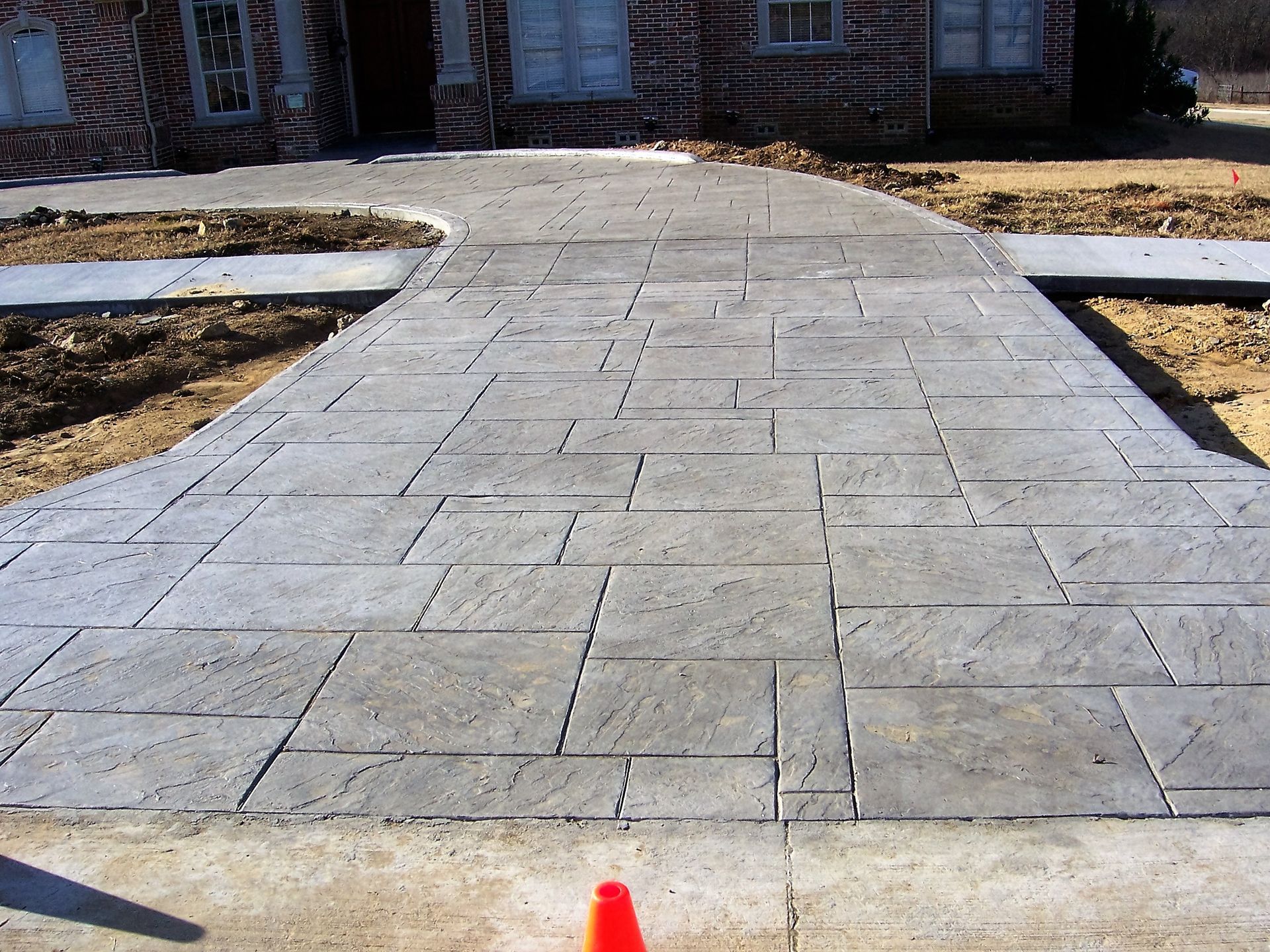 Concrete walkway with stone pattern leading to a brick house.