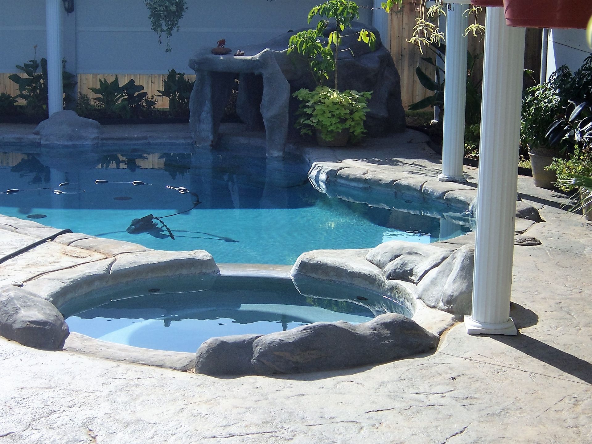 Swimming pool with rock features and a hot tub, surrounded by a concrete patio.