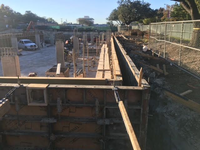 Construction site with wooden forms, concrete pillars, and a fence in the background.