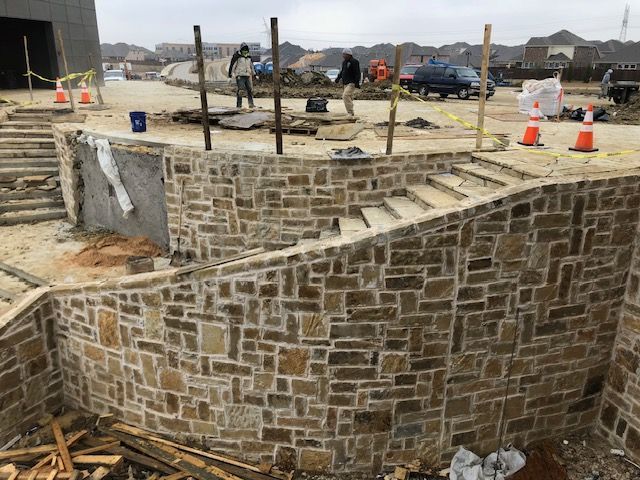 Construction site with stone retaining wall, steps, and workers; outdoors.