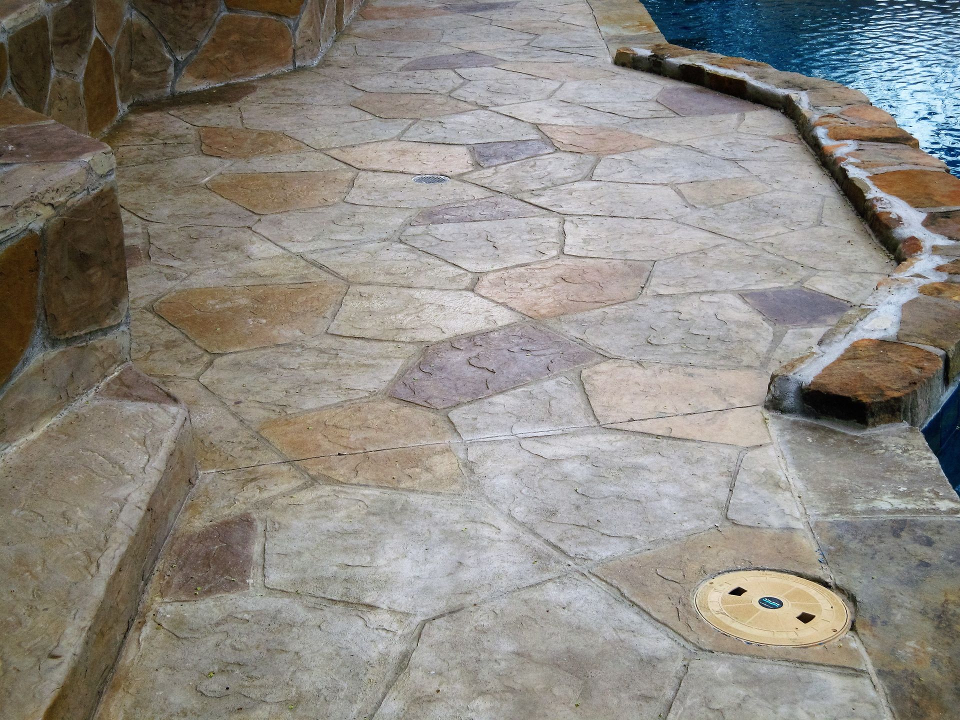 Gray pergola with stone fireplace, seating, and landscaping on patio with garden.