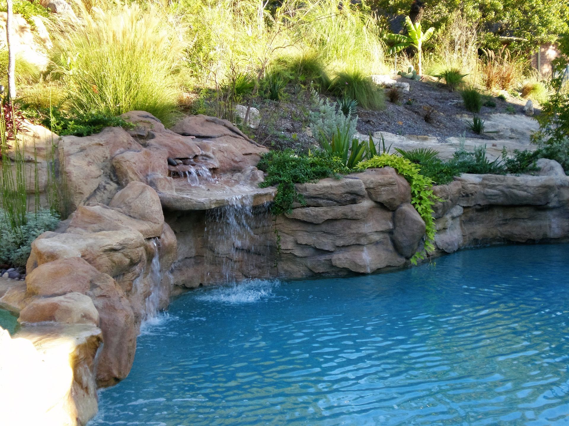 Waterfall cascading into a turquoise pool, surrounded by rock formations and greenery.