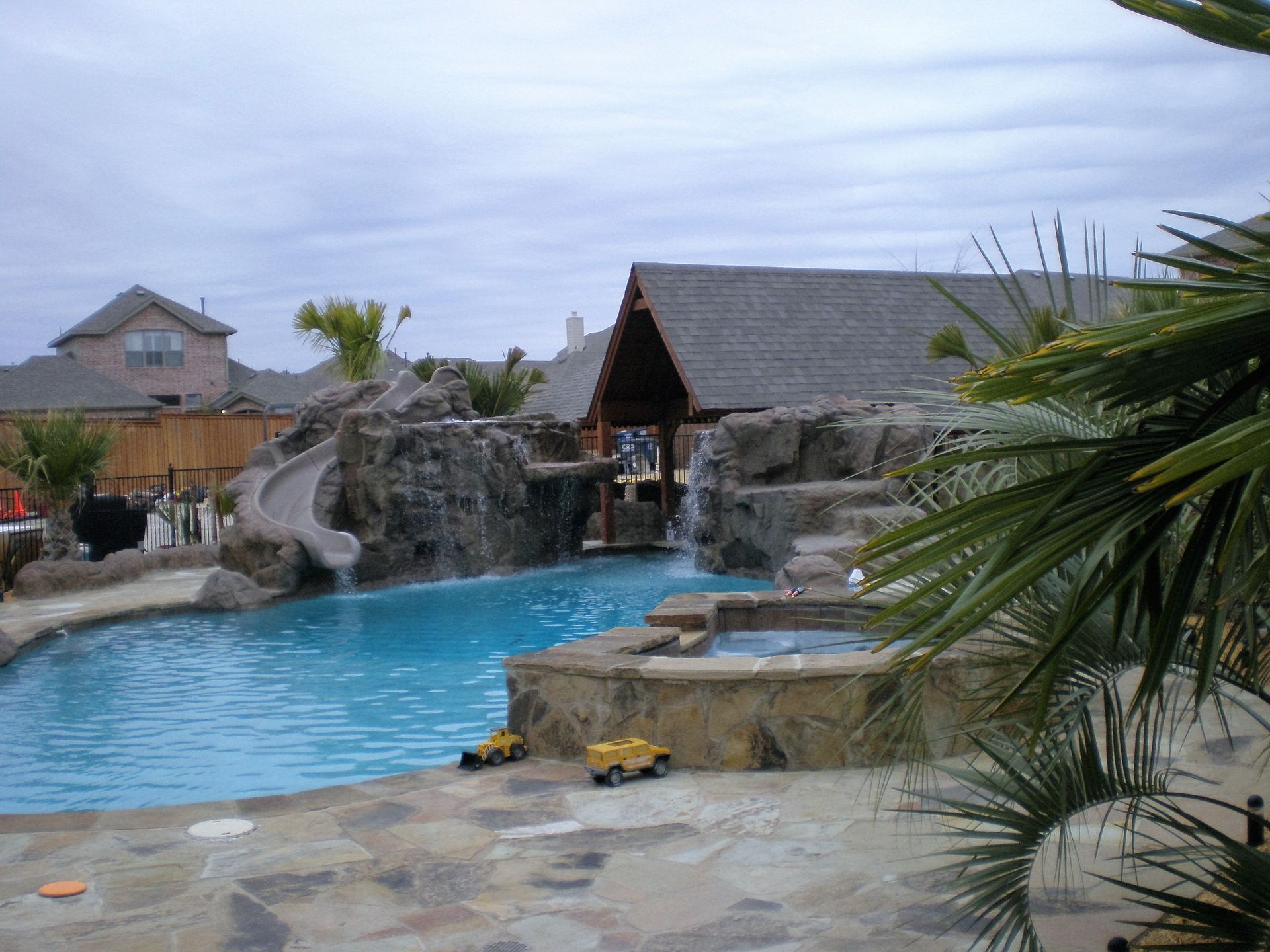 Swimming pool with a rock waterfall, slide, and covered outdoor kitchen.