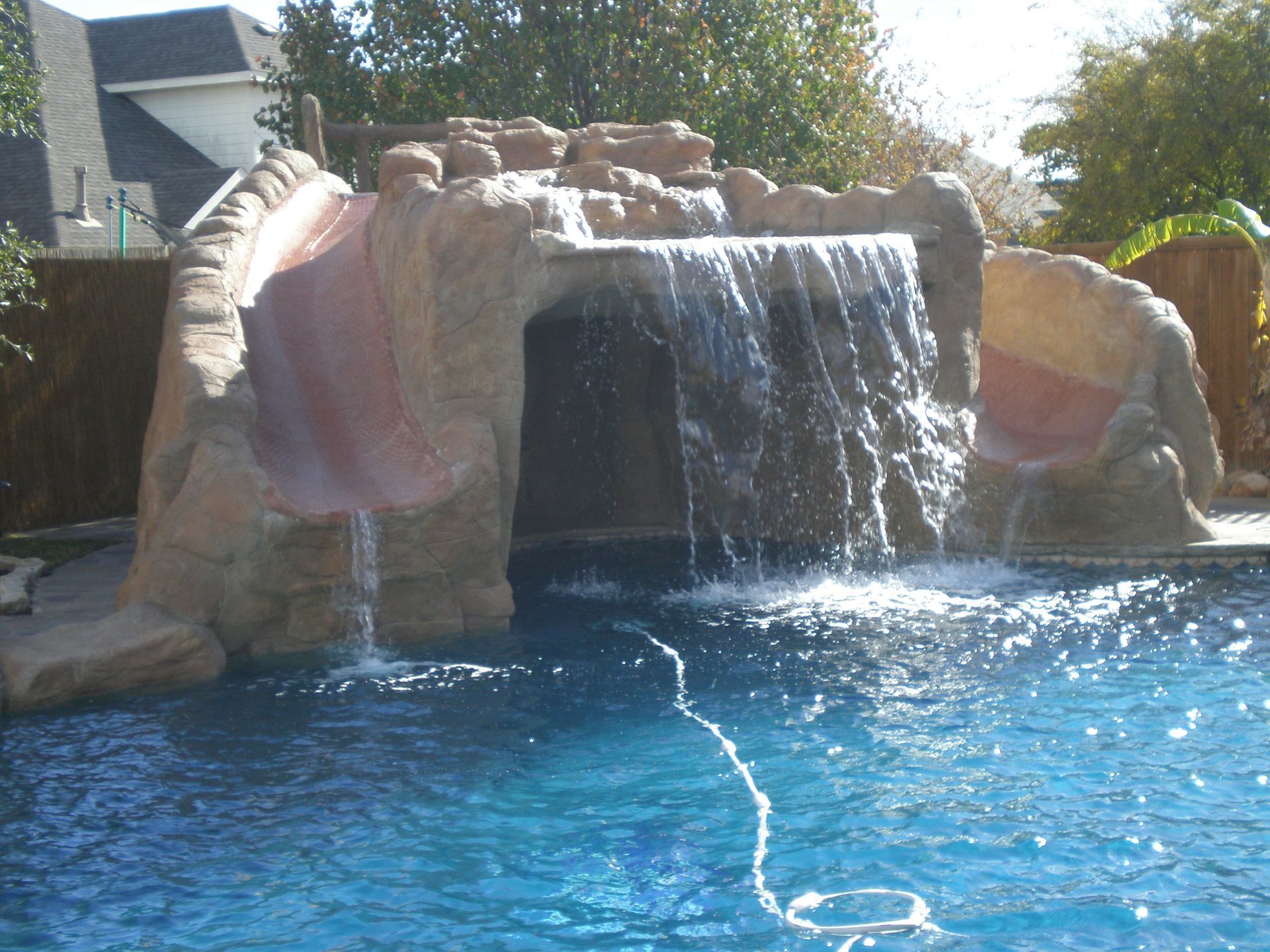 Pool with rock waterfall feature and slide. Clear blue water and sunny setting.