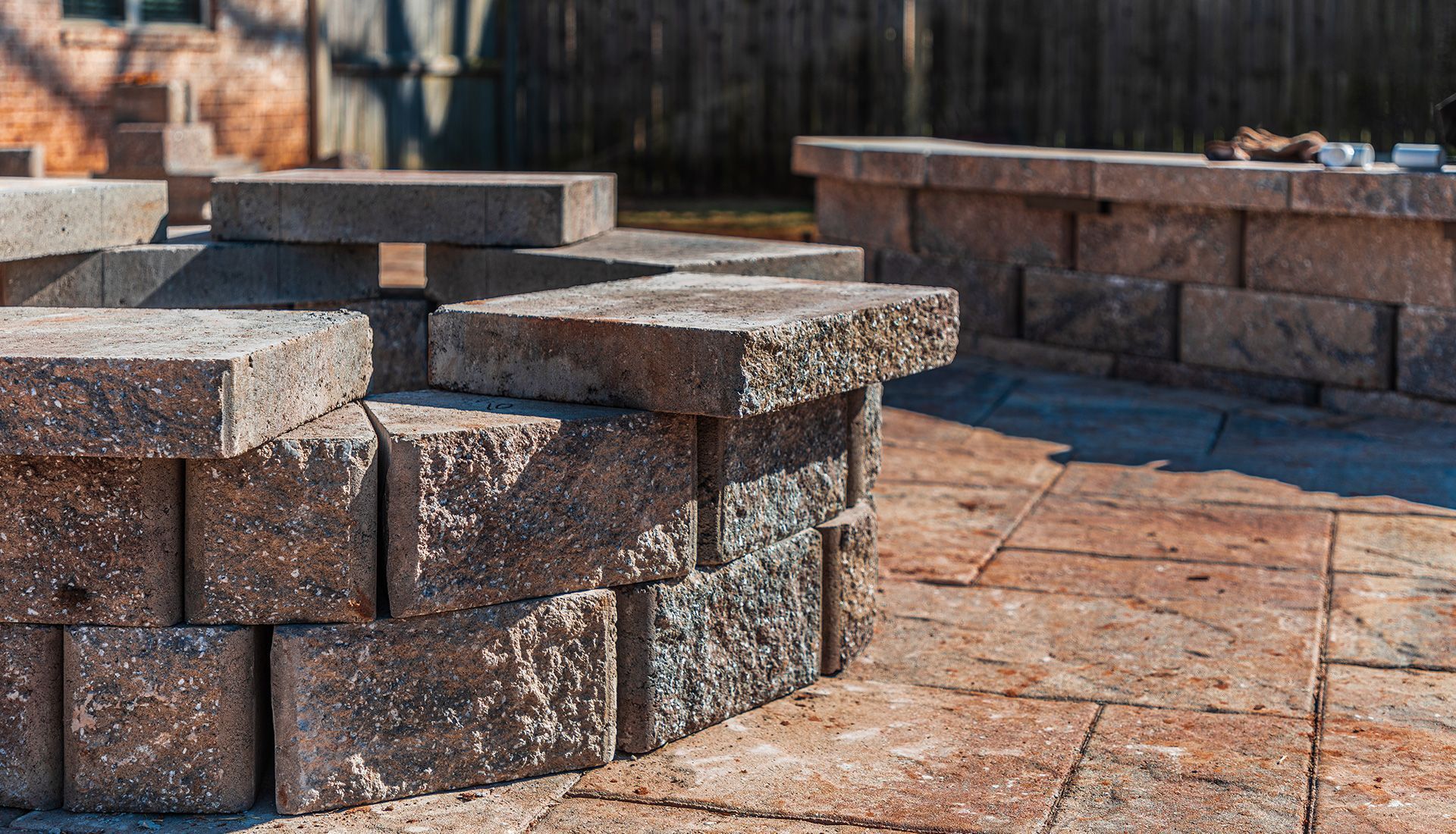 Stone fire pit and low wall being built on a patio; brown and gray tones.