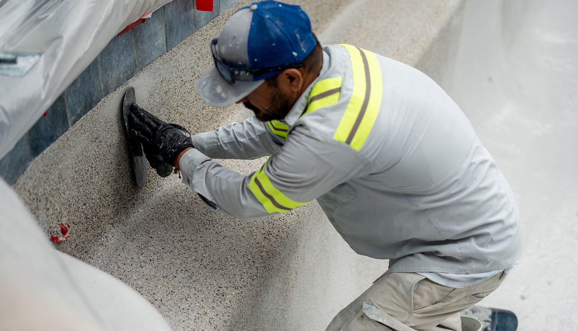 Construction worker laying dark gray paving stones, wearing orange gloves.