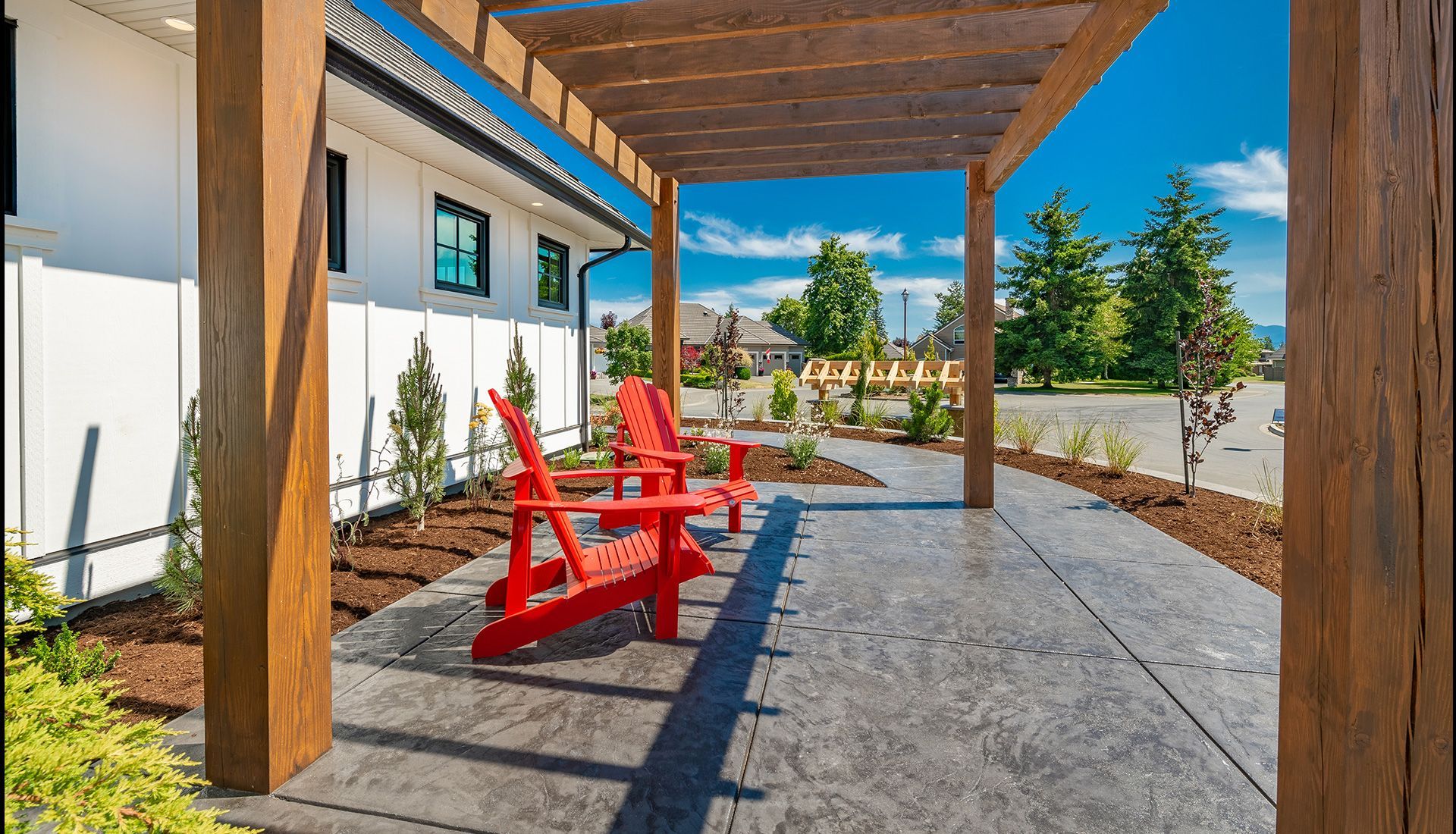 Red Adirondack chairs under a wooden pergola on a concrete patio.
