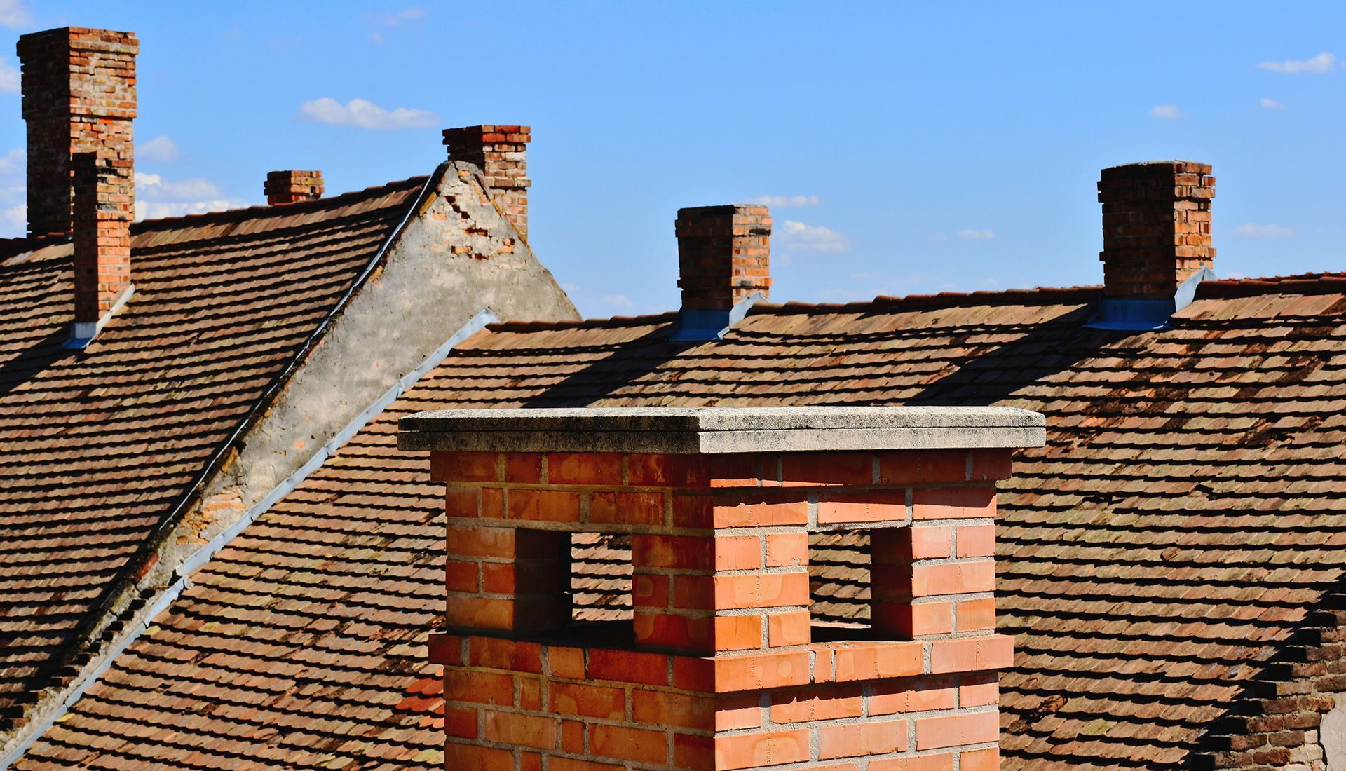 Brick chimneys on a weathered, tiled roof under a blue sky.