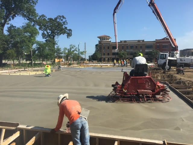 Construction workers smoothing concrete with a machine; outdoor site, sunny day.