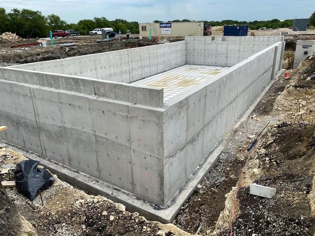 Concrete foundation of a rectangular structure under construction in a dirt lot.