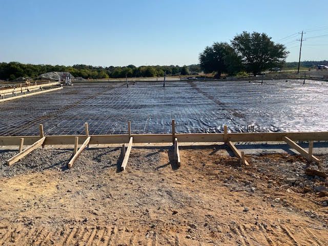 Newly poured concrete foundation with rebar, wood forms, and stakes on a construction site.
