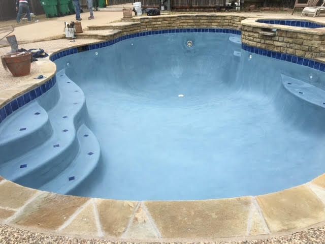 A newly plastered swimming pool with blue tile and stone coping.