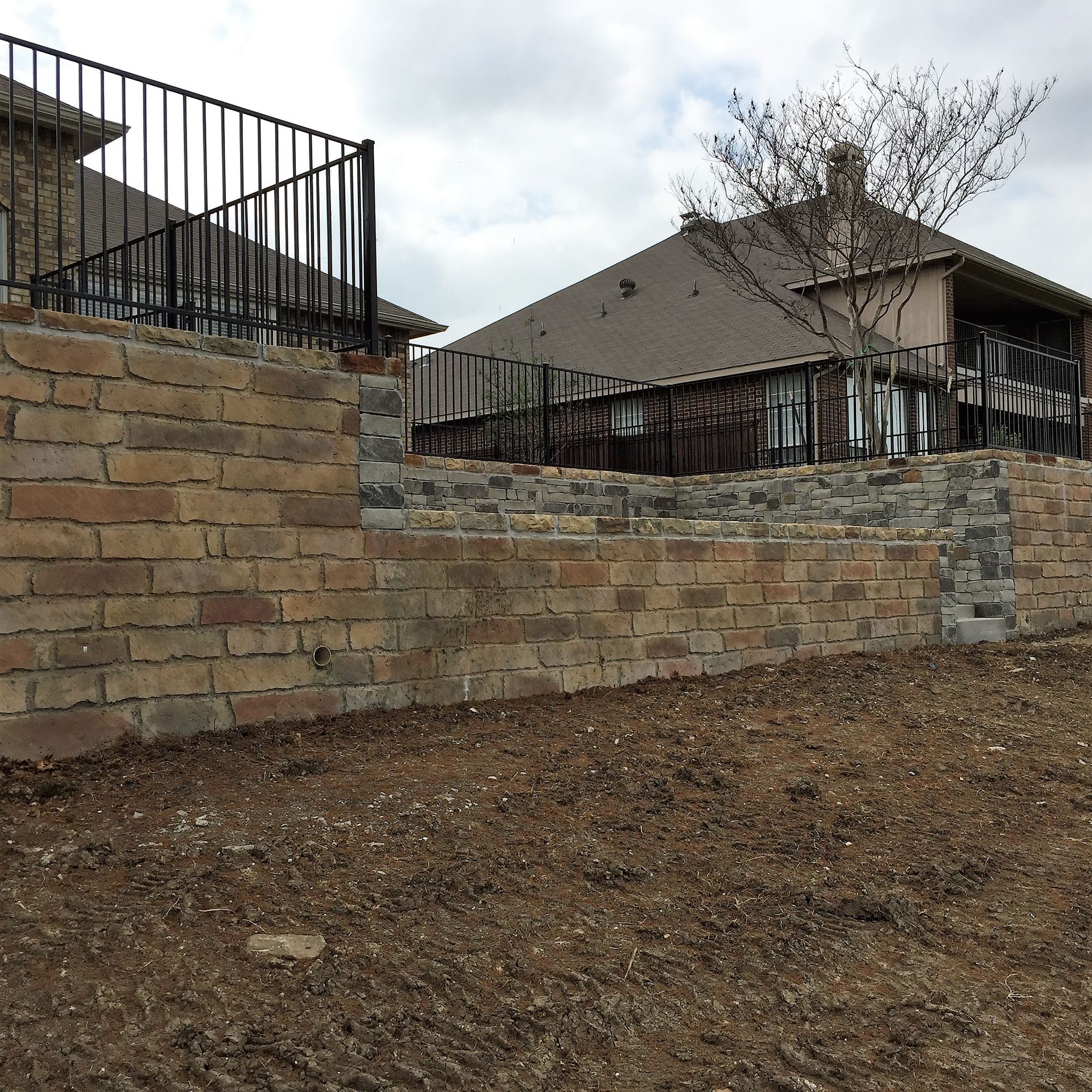 Stone wall with varying sizes and shapes, gray and brown tones, with green foliage in the background.