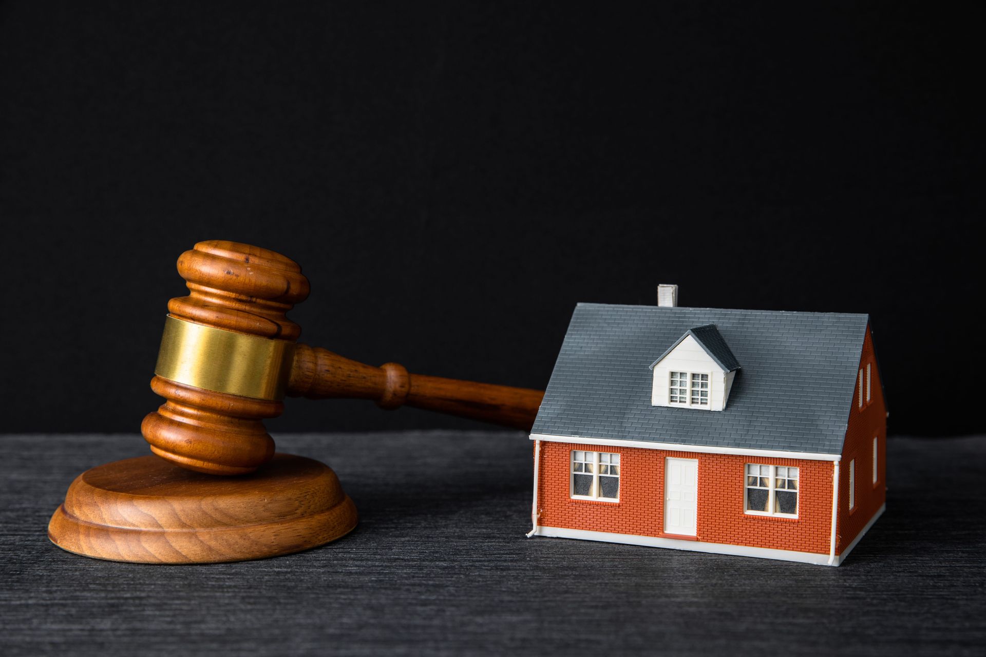 Gavel beside a small house model on a dark surface, symbolizing housing law or foreclosure