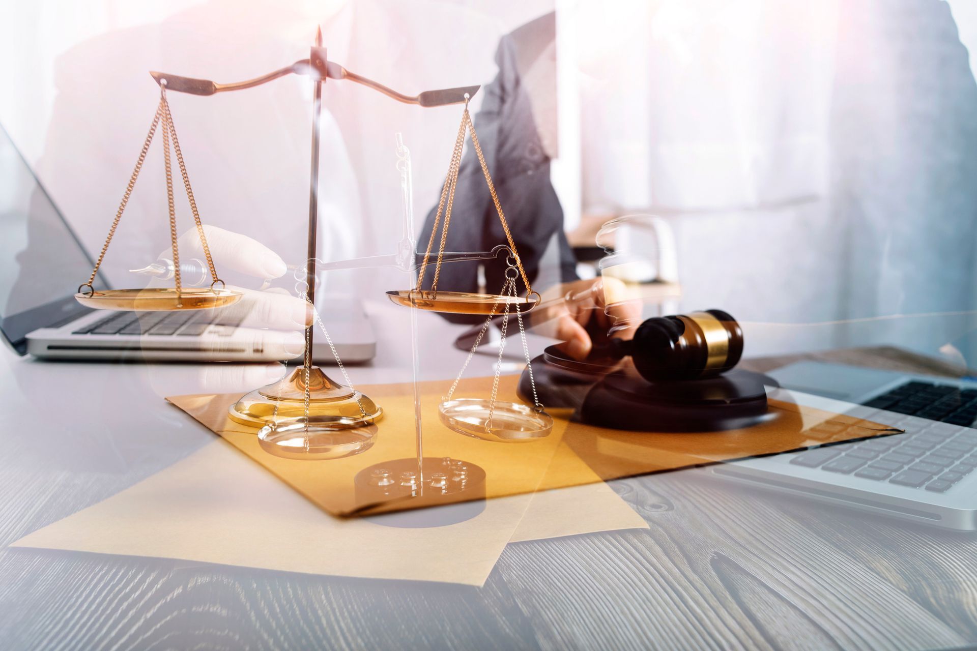 A gold scales of justice and a wooden gavel resting on a document on a desk next to a laptop.