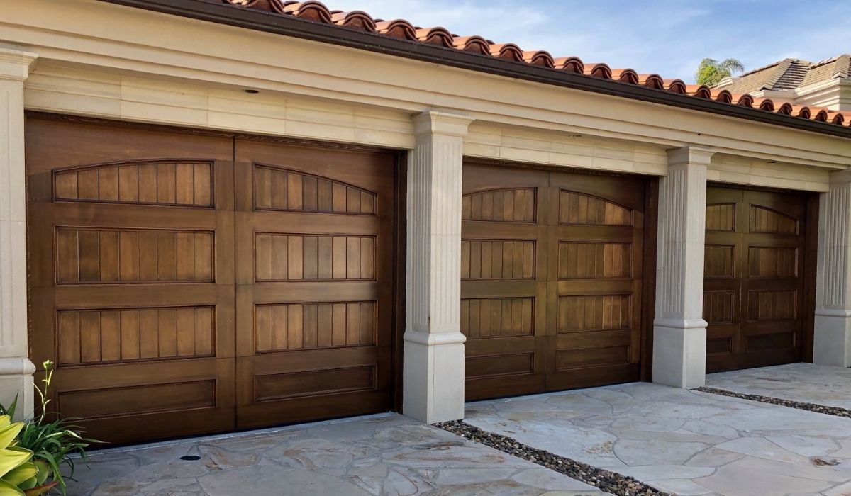 Three wooden garage doors beneath a stucco roof with white columns